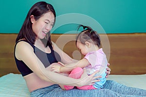 Little daughter Sitting on the mother`s lap A beautiful Asian lady mother is pregnant. happily
