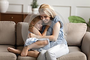 Little daughter and young mommy hugging on couch