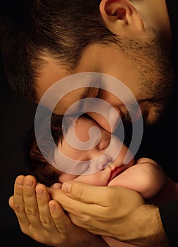 Little 15 days old baby lying securely on his Dad`s arms, against a black background