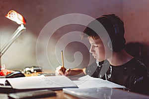 LIttle diligent boy doing his homework while listening music by headphones