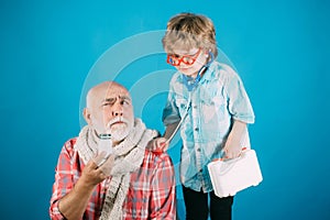 Little doctor ready to examine. Charming little boy examining a cheek of his grandfather. Old man with scarf holding a