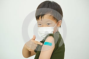 Little doubtful kid wearing medical mask showing his arm with bandage after receiving vaccination