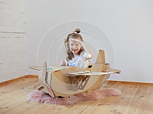 Little dreamer girl playing with a cardboard airplane. Childhood. Fantasy, imagination.