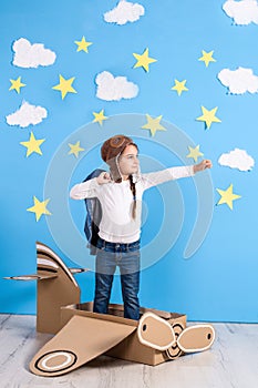 Little dreamer girl playing with a cardboard airplane at the studio with blue sky and white clouds background.