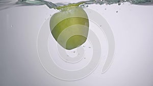 LIttle drop of water falling down from the fresh green apple into the water with small circular waves and little splash