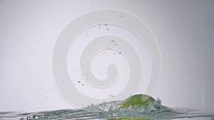 LIttle drop of water falling down from the fresh green apple into the water with small circular waves and little splash