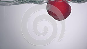 Little drop of water falling down from the fresh red apple into the water with small circular waves and little splash
