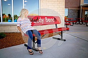 Little Elementary School Aged Child Sitting Alone on A Buddy Bench at School