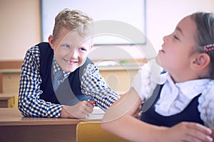 Little elementary school student boy tries to disturb the girl during the lesson. Boy tries to reach the girl`s back