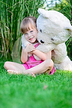 Little elfin girl sittinging in the grass with large teddy bear