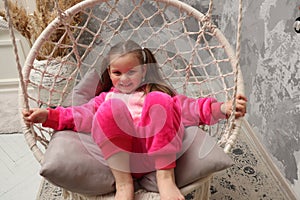 Little emotional girl rides on a swing in the children& x27;s room. Happy child 4-5 years old close-up. A small child