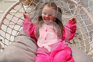 Little emotional girl rides on a swing in the children& x27;s room. Happy child 4-5 years old close-up. A small child