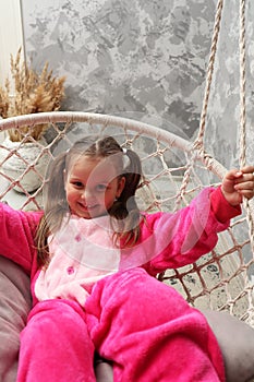 Little emotional girl rides on a swing in the children& x27;s room. Happy child 4-5 years old close-up. A small child