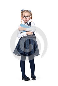 Little emotional girl in a school uniform with glasses stands with a book pouting cheeks, isolated on white background.