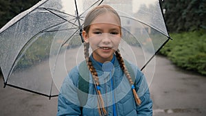 Little European girl looking at camera smiling holding umbrella rain weather park walk outside daughter child learner