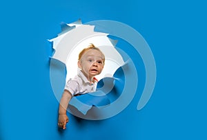 Little explorer. Little kid cutting through blue wall. Curious boy child look out of hole in paper. Little child peek