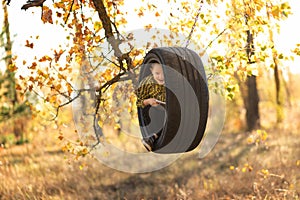 Little fair-haired boy with a smile holds a book in a swing wheel