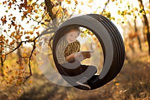 Little fair-haired boy with a smile holds a book in a swing wheel
