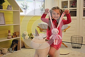 A little fair-haired European girl in pink clothes plays with plush toys in a bright children& x27;s room. A pink