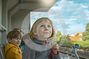 A little fair-haired girl with a flower in her hand looks dreamily and sadly at the sky