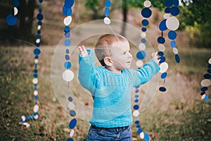 Little fashion boy in a forest wearing blue sweater and jeanse