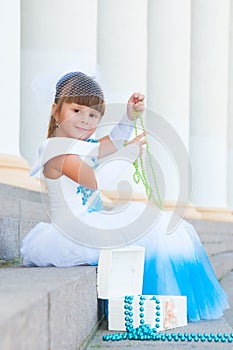 Little fashion-girl in magnificent blue and white evening dress sitting on the steps near the colonnade
