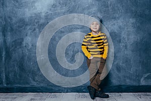 Little fashionable boy posing in front of a gray-blue concrete wall. Portrait of a smiling child dressed in a black and yellow