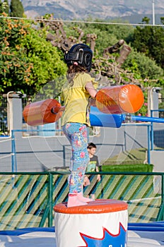 Little Female Kid Plays American Gladiator and Swings the Stick. Young Girl Playing Joust Game