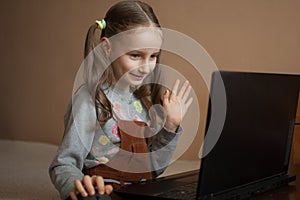 Little female pupil is studying at home with her teacher using video chat on her black laptop because of the self