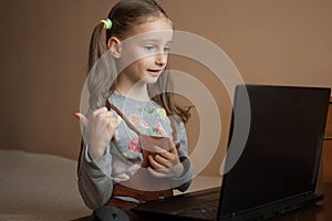 Little female pupil is studying at home with her teacher using video chat on her black laptop because of the self