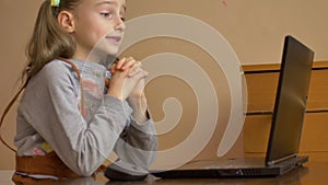 Little female pupil is studying at home with her teacher using video chat on her black laptop because of the self