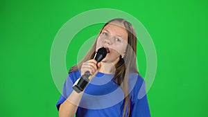 Little female singing into microphone on green screen at studio