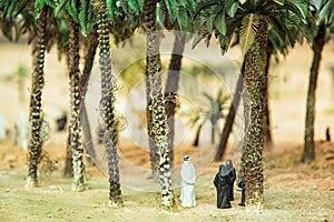 Little figurines of Arabs in the desert oasis under the palm trees