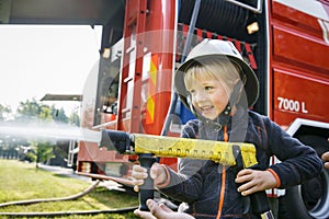 Little fireman holding firehose nozzle and splashing water