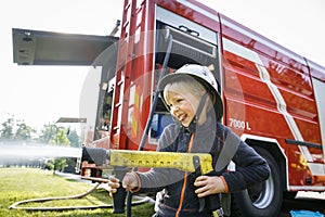 Little fireman holding firehose nozzle and splashing water