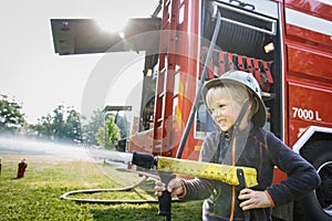 Little fireman holding firehose nozzle and splashing water