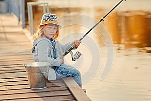 Little fisher girl smiles sitting near a river with a rod