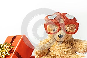Little fluffy teddy bear wearing red heart shaped glasses and holding red balloon. Happy Valentine's Day. Presents in a red