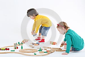 Little focused boy and girl build railway from wooden parts