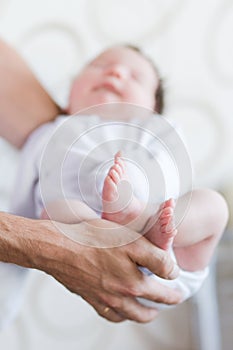 Little foot in hand. Father holding the legs of a newborn in his hands. Mom cares for the baby after taking a bath. Parents to