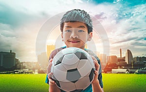 Little football boy with smile is holding a soccer ball with city background