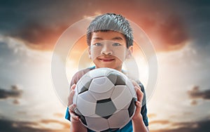 Little football boy with smile holding a soccer ball with golden sky background