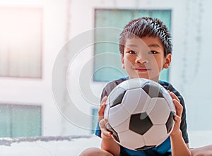 Little football boy with smile is holding a soccer ball while playing indoor at home