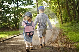 Little friends children hold hands and walk along path in park on summer day. boy and girl are walking in park outdoors