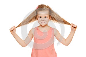 Little fun joyful girl in a pink shirt holds hands hair, isolated on white background