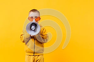 Little fun kid boy 3-4 years old in yellow clothes holding, speaking in electronic megaphone isolated on orange wall