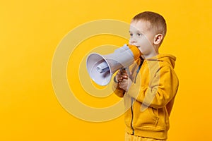 Little fun kid boy 3-4 years old in yellow clothes holding, speaking in electronic megaphone isolated on orange wall