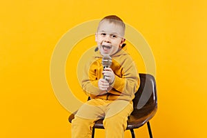 Little fun kid boy 3-4 years old in yellow clothes sing song in microphone isolated on bright orange wall background photo