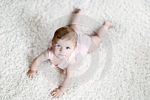 Little funny baby girl lifting body and learning to crawl.