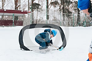 Little funny boy with her mother skating in the park. Play ice hockey with stick and goal. Outdoor. Winter sport